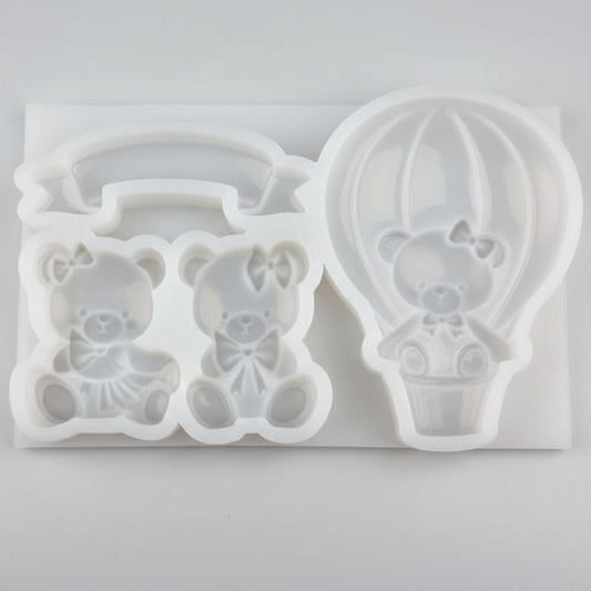 Molde de silicona blanco para repostería con figuras de globo aerostático de 7 cm, dos ositos de 4 cm y un banner decorativo. Incluye ejemplo de figuras terminadas en color rosa pastel.