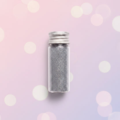 Escarcha comestible glitter plateado en frasco de vidrio con tapa metálica 10 gr sobre fondo bokeh rosa – glitter para repostería - Vallia Reposteria