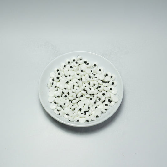 Plato con abundantes ojos comestibles pequeños de azúcar, blancos con pupila negra, para decoración de personajes en repostería. Paquete de 50 gramos de ojitos dulces.