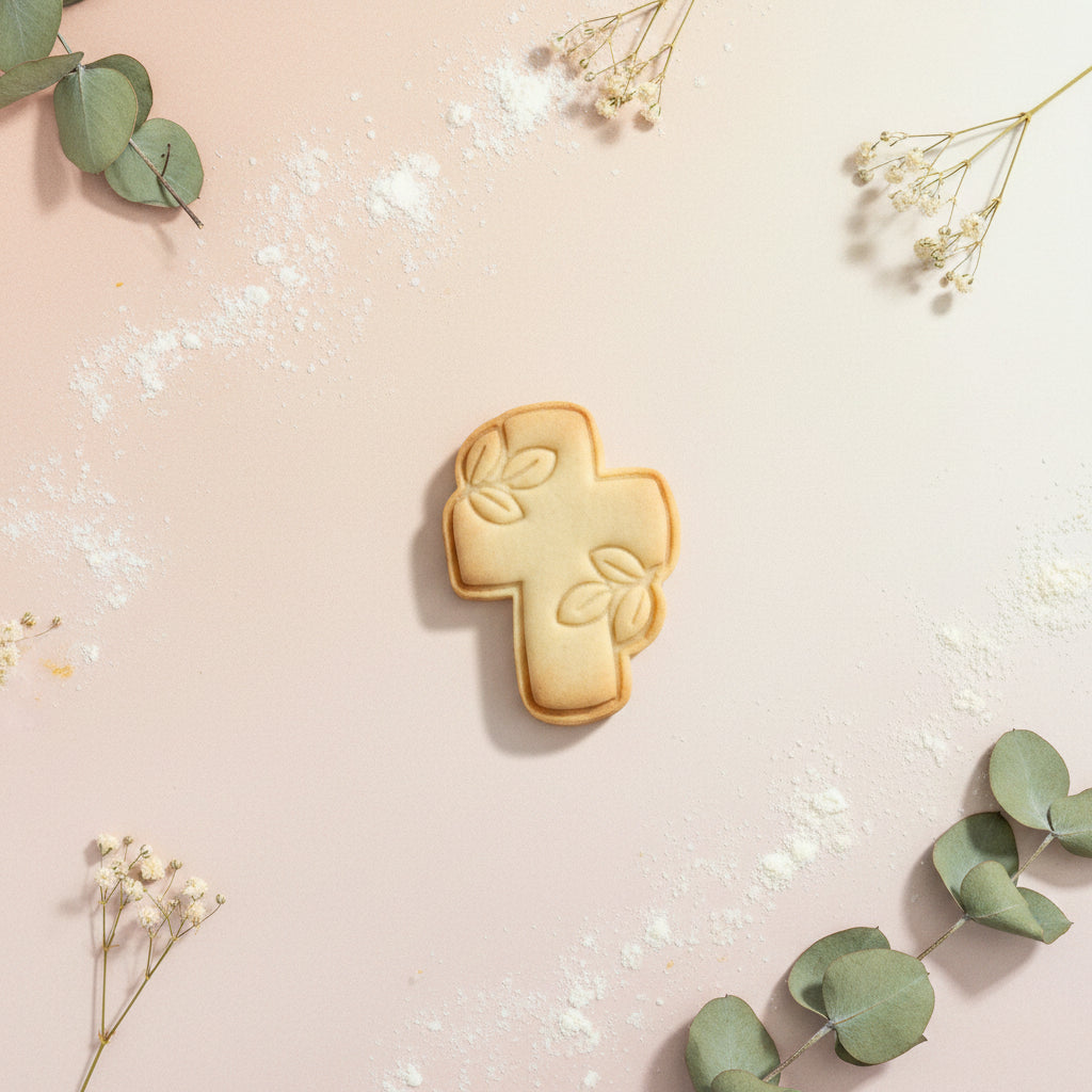 Cortador con sello marcador para galletas modelo cruz floreada 8 cm con galleta sin decorar sobre fondo rosa con eucalipto y flores secas – para bautizos y comuniones - Vallia Reposteria