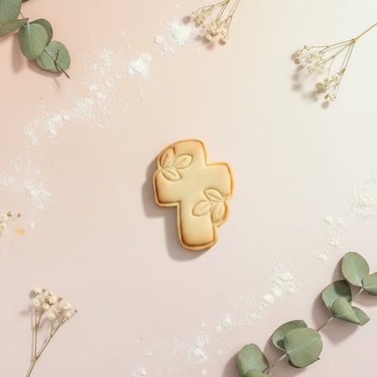 Cortador con sello marcador para galletas modelo cruz floreada 8 cm con galleta sin decorar sobre fondo rosa con eucalipto y flores secas – para bautizos y comuniones - Vallia Reposteria