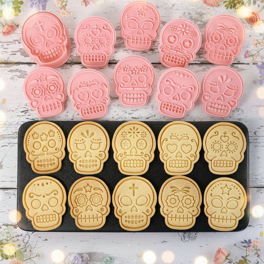 Set de 10 sellos marcadores de calaveras mexicanas en plástico rosa con 10 galletas horneadas con diseños surtidos de catrina sobre bandeja negra – para Halloween y Día de Muertos - Vallia Reposteria