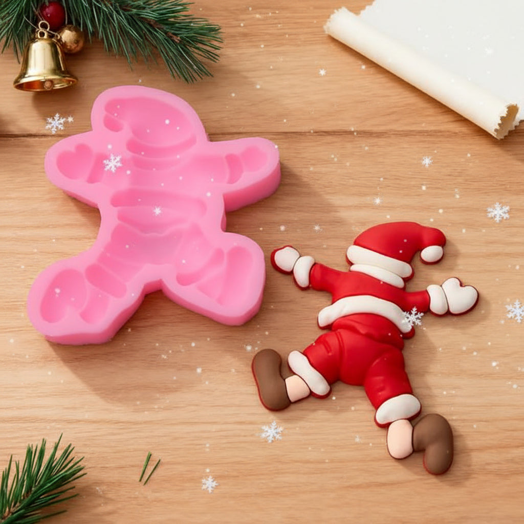 Molde de silicona rosa de Papá Noel caído 9.1x8.2 cm junto a figura terminada en fondant rojo blanco y marrón sobre mesa de madera con ramas de pino y campana dorada - Vallia Reposteria