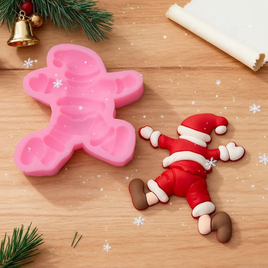 Molde de silicona rosa de Papá Noel caído 9.1x8.2 cm junto a figura terminada en fondant rojo blanco y marrón sobre mesa de madera con ramas de pino y campana dorada - Vallia Reposteria