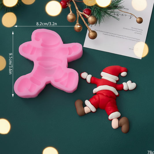 Molde de silicona rosa de Papá Noel caído con medidas 8.2x9.1 cm junto a figura terminada en fondant sobre fondo verde oscuro con luces bokeh y decoración navideña - Vallia Reposteria