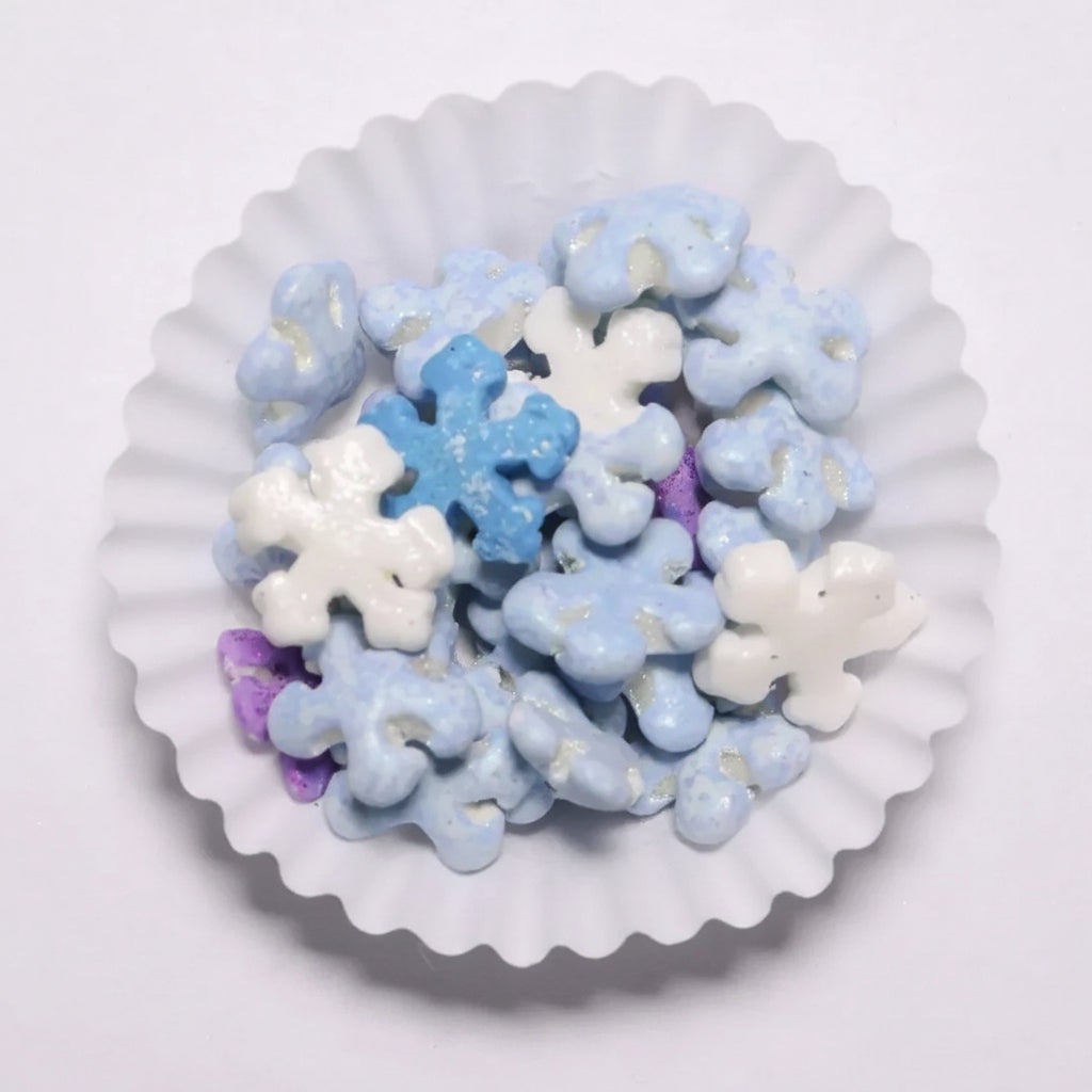 Gragea Navideña de Vallia Repostería con forma de copos de nieve en tonos azul, blanco y morado en capacillo blanco.